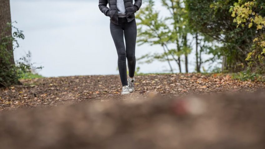 A woman walks along a scenic forest trail during autumn, capturing the essence of outdoor leisure and fitness.